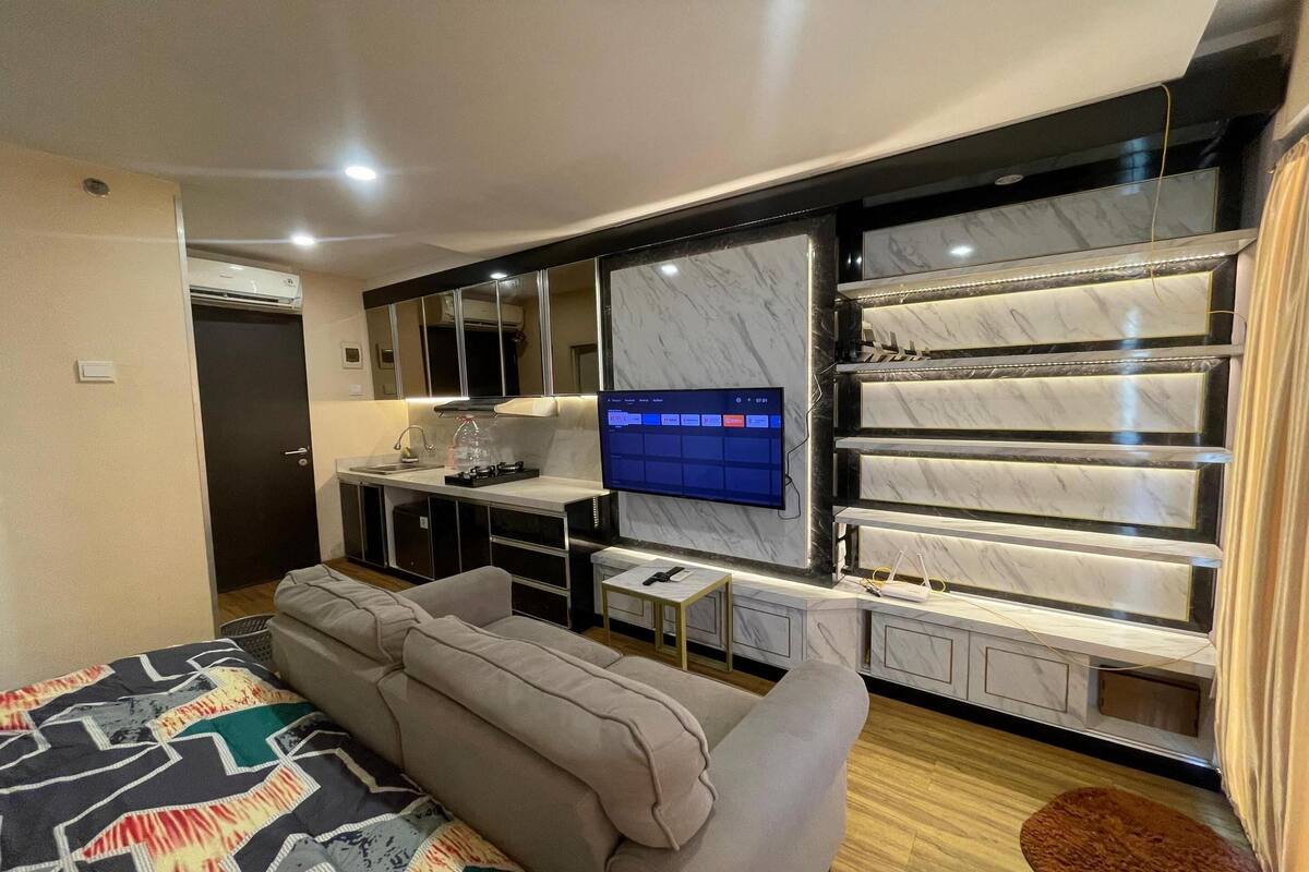 Une chambre d’hôtel moderne dotée d’un grand lit, d’un canapé, d’un téléviseur fixé au mur (qui est recouvert de marbre) et d’un mini-bar.