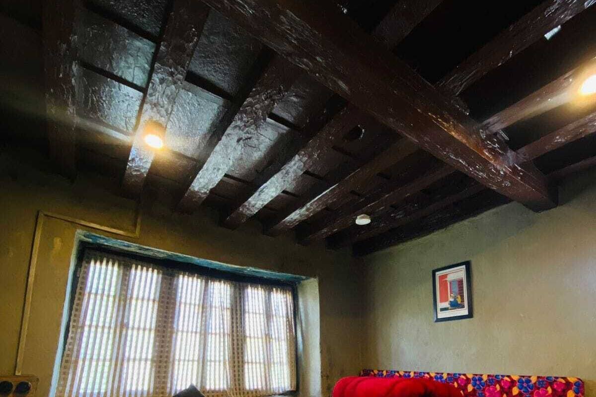 A room with a wooden ceiling, a window with blinds, a bed with a colorful headboard, and a patterned rug.