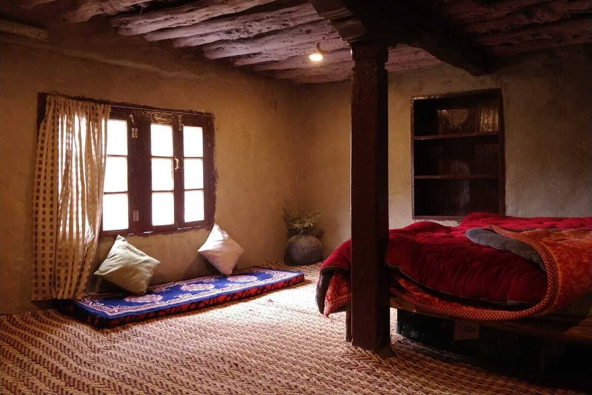A cozy room with a bed, a window with curtains, a bookshelf, and a rug.