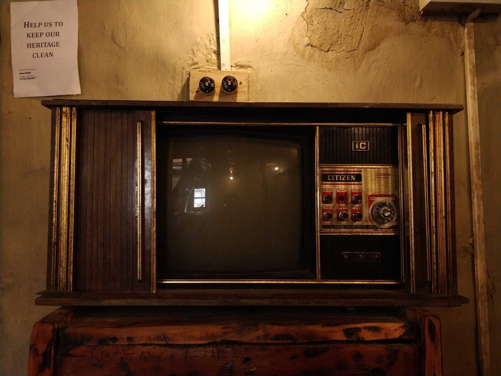 Μια παλιά τηλεόραση τοποθετημένη πάνω σε ένα ξύλινο έπιπλο, με μια επιγραφή ακριβώς από πάνω.