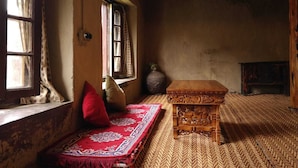 Une pièce au décor traditionnel, avec un tapis tissé, une table en bois ornée de sculptures et un grand vase.