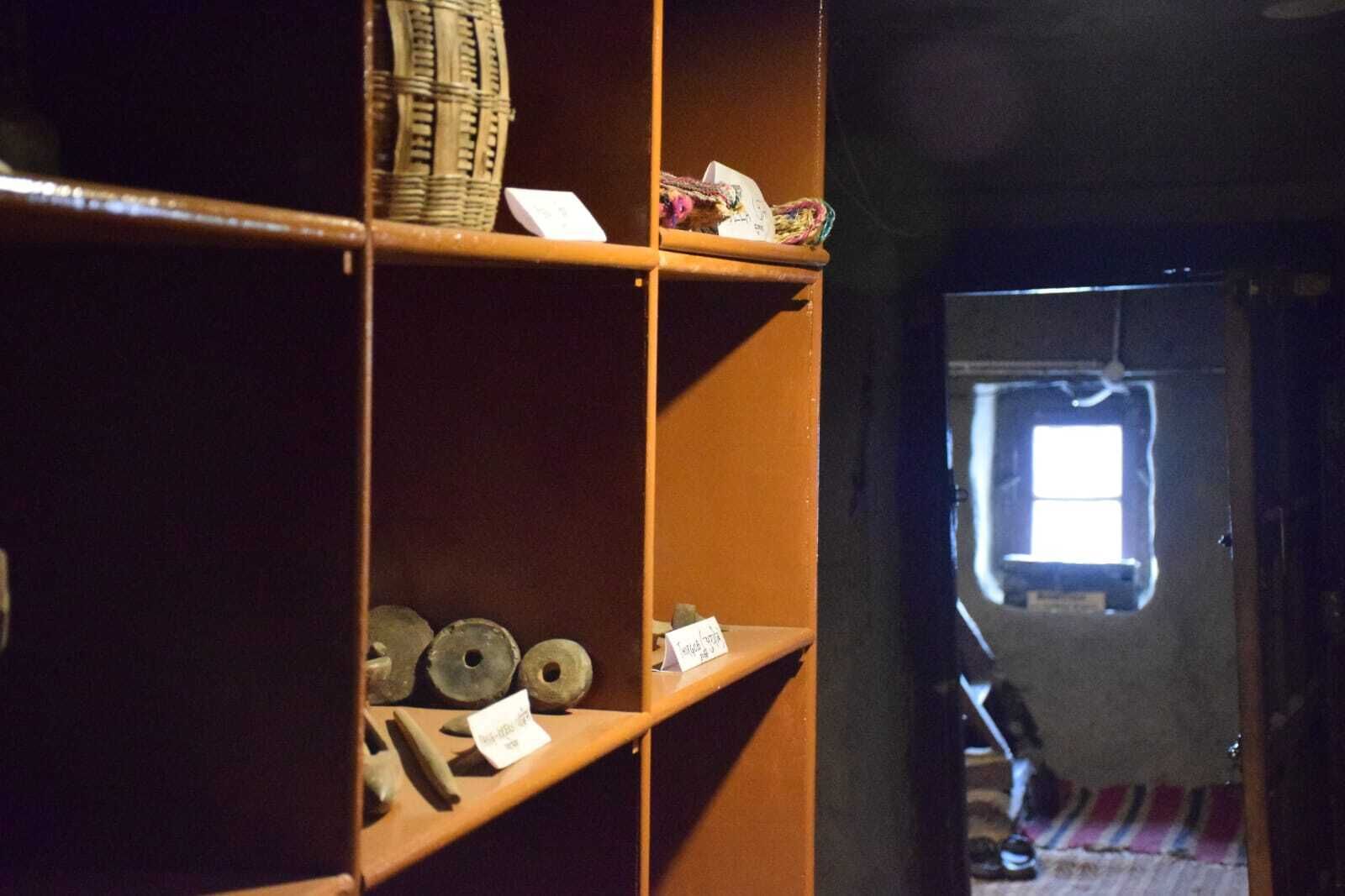 A room with wooden shelves displaying various items, a wicker basket, and a small window with natural light.