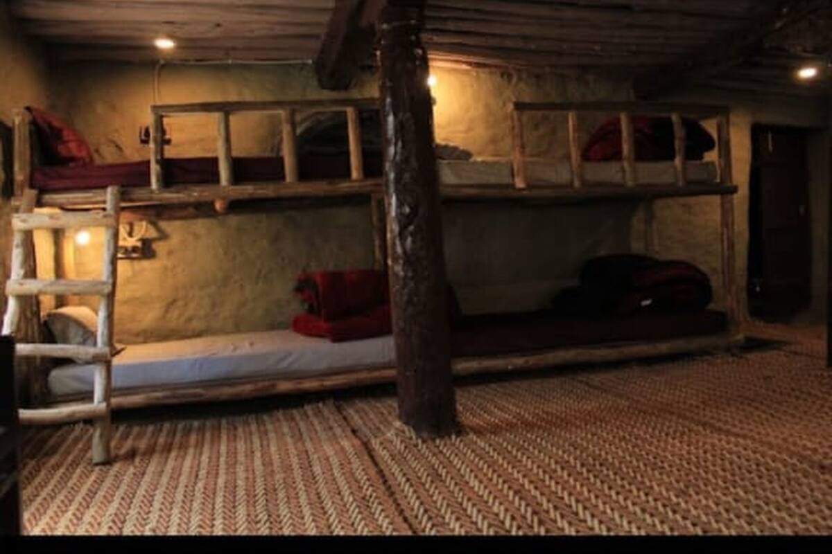 A rustic room with a bunk bed, a wooden ladder, and a woven floor mat.