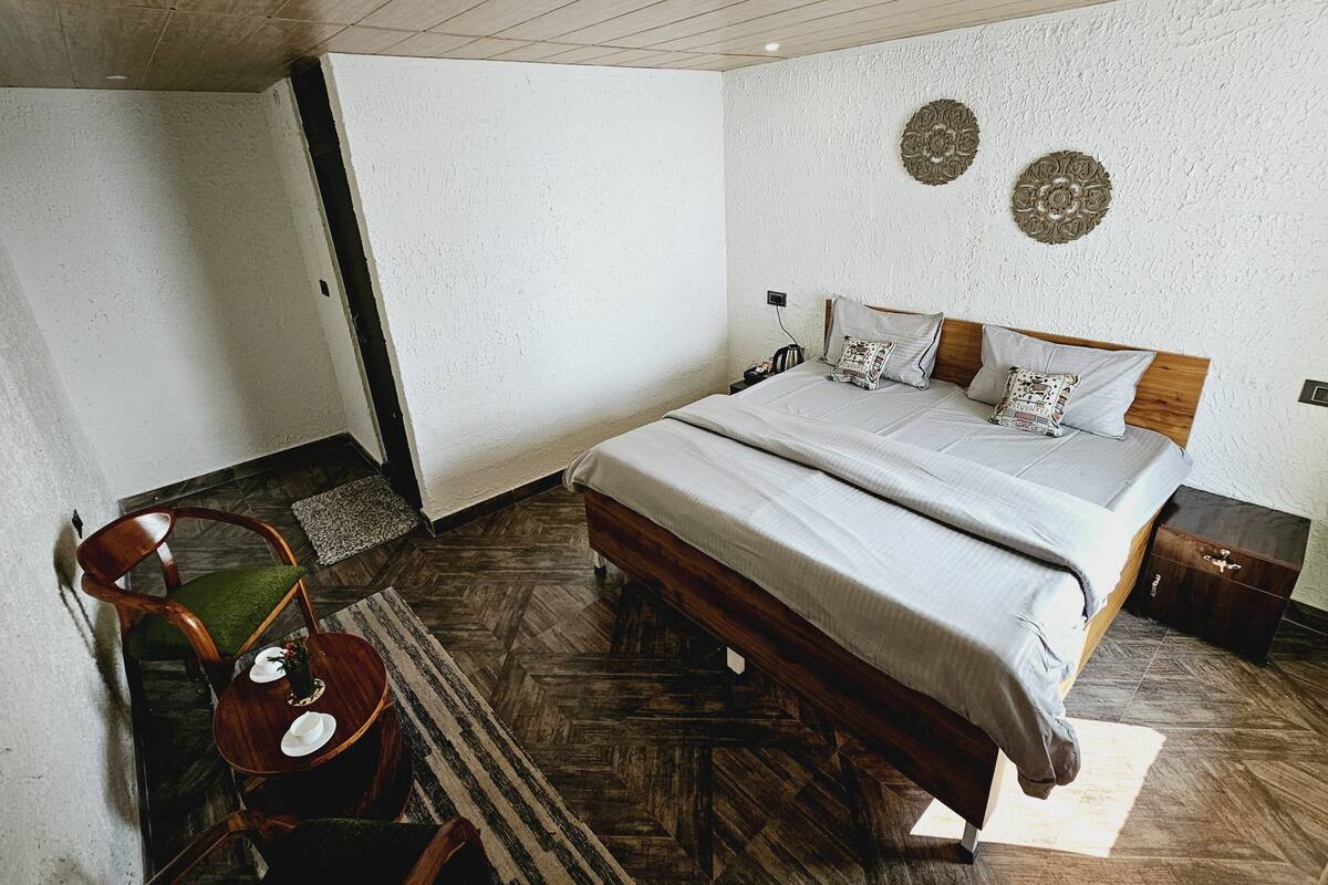 A bedroom with a wooden bed, a chair, a small table, and a rug.