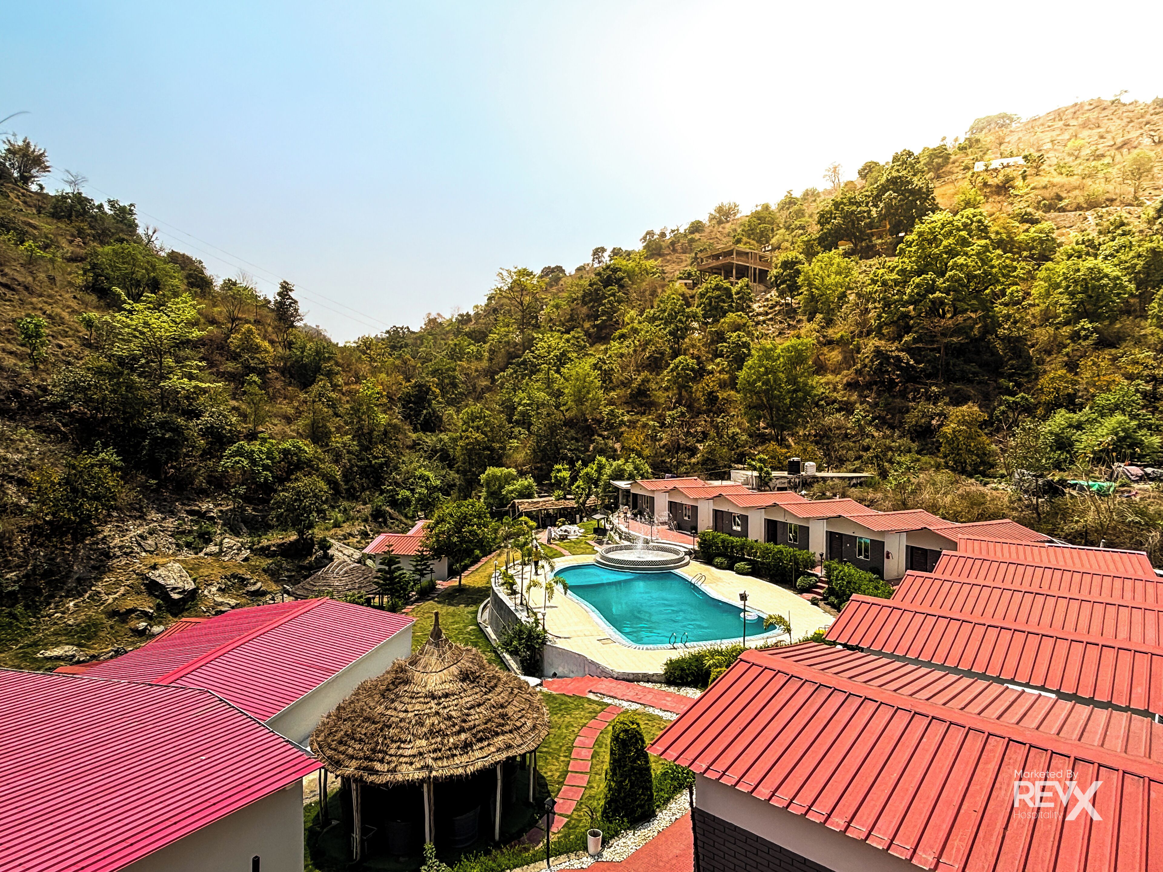 Un resort con varias edificaciones, una piscina y una estructura de techo de paja.