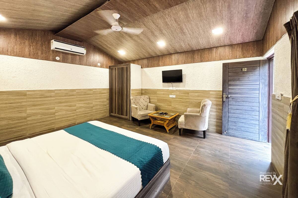 Ein Schlafzimmer mit einem Bett, zwei Stühlen, einem kleinen Tisch, einem Fernseher und einer Tür.