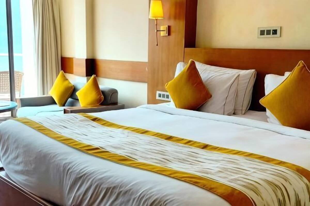 Ein Hotelzimmer mit einem großen Bett, einem Nachttisch, einer Lampe und Blick ins Freie.