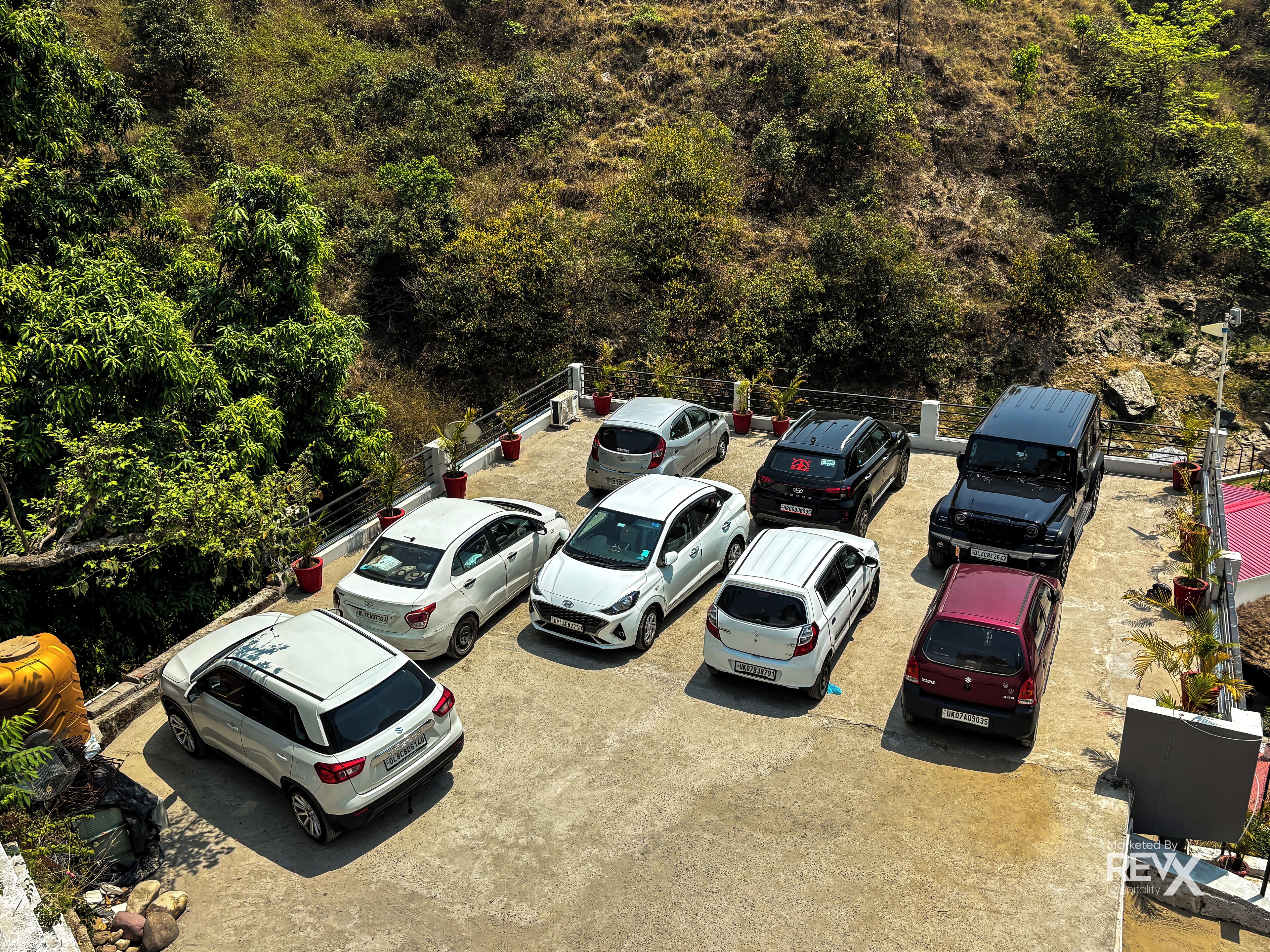 Ein Parkplatz mit mehreren Autos auf einer abschüssigen Fläche, umgeben von Grünflächen und Bäumen.