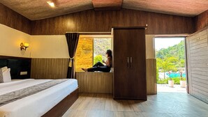 A bedroom with a bed, a wardrobe, a window with curtains, and a view of the outdoors. - Anandvan Jungle Resort (Rishikesh)