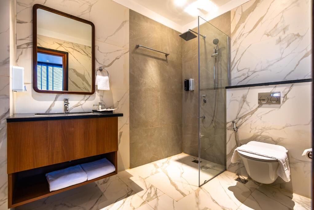 A modern bathroom with a marble floor, a wooden vanity, a glass shower enclosure, and a toilet.