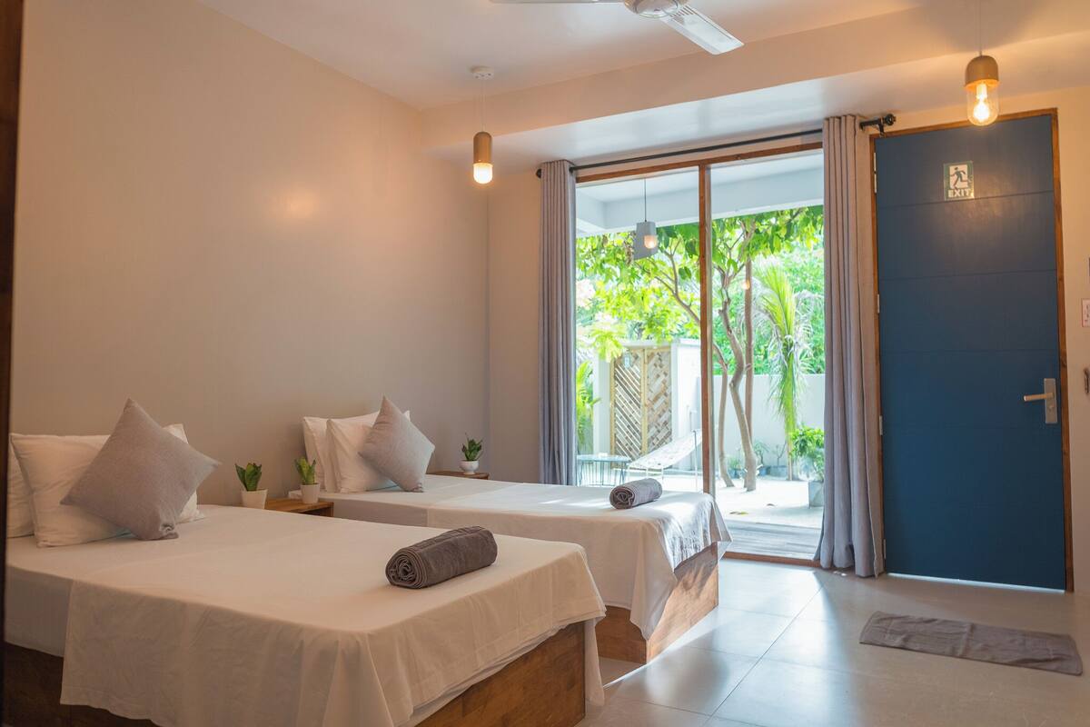A hotel room with two beds, a sliding glass door to the outside, and a ceiling fan.