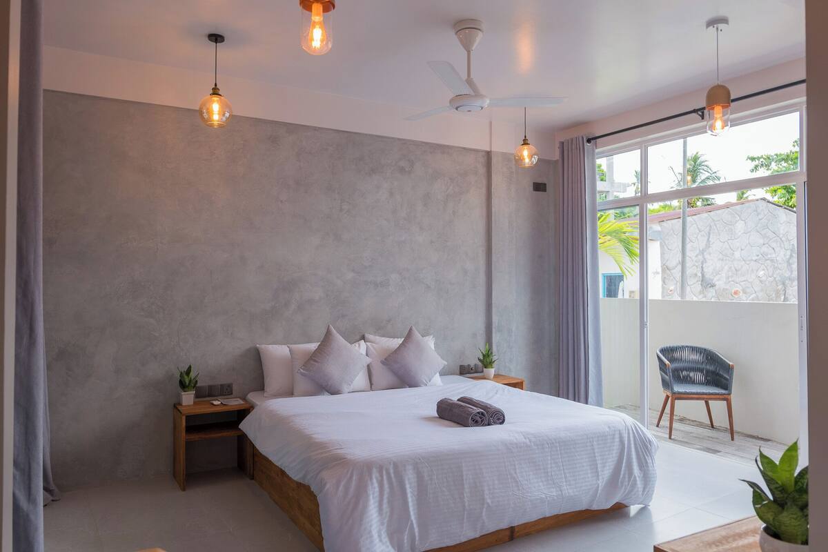 A modern bedroom with a large bed, a ceiling fan, and a view of the outdoors.