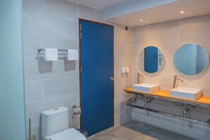 Une salle de bain moderne avec une porte bleue, deux lavabos, un miroir et des toilettes.