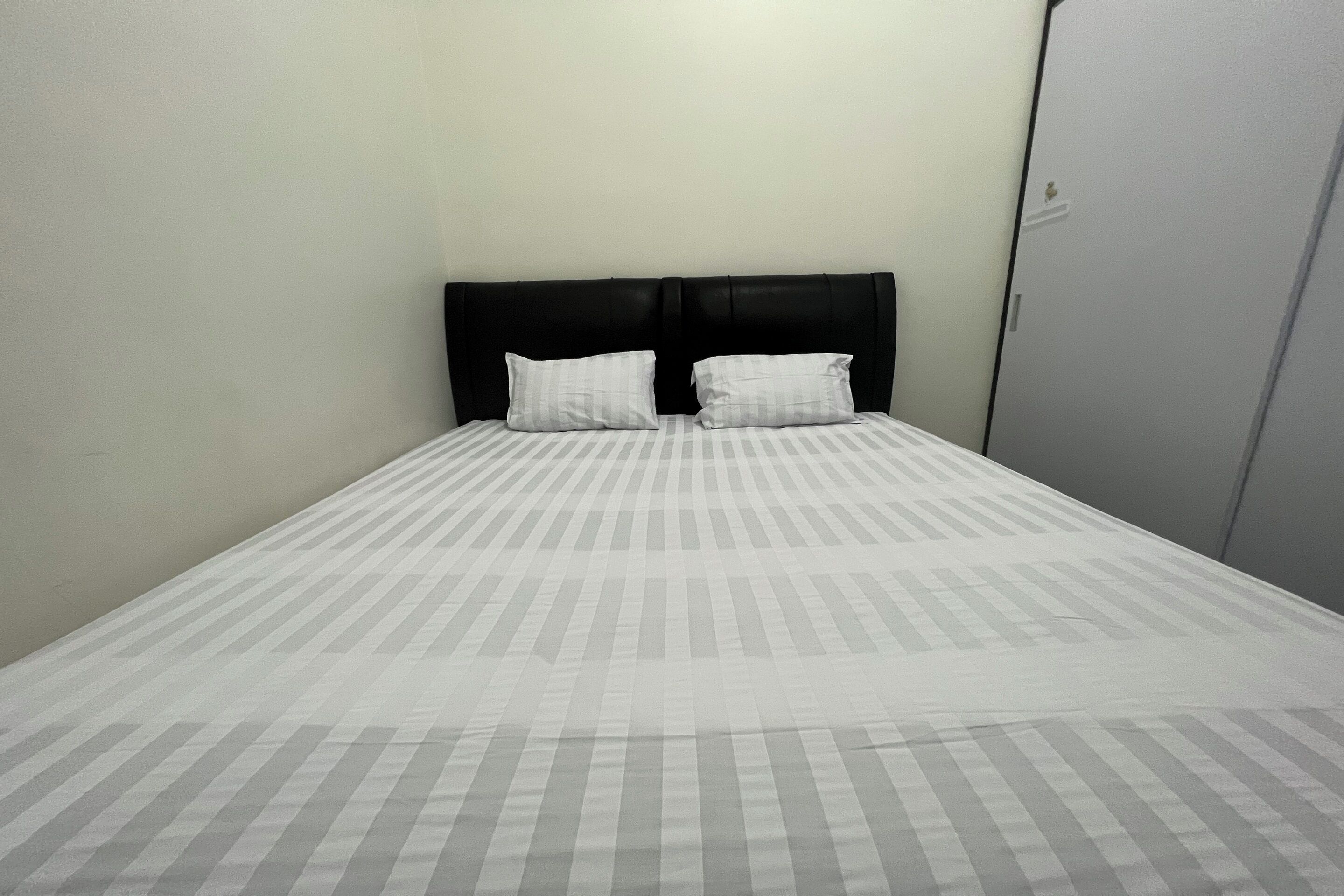 A single bed with a black headboard and two pillows, a plain wall, and a door to the right.
