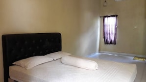 Ein Einzelbett mit dunklem Kopfteil und weißer Bettwäsche in einem Zimmer mit beigen Wänden und einem Fenster mit violetten Vorhängen.