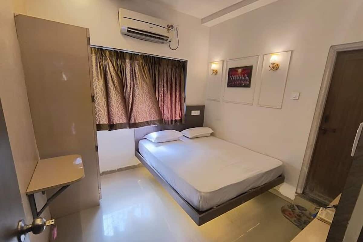 Une chambre d’hôtel comprenant un lit, un appareil de climatisation, une fenêtre avec des rideaux, une table de chevet et une porte.