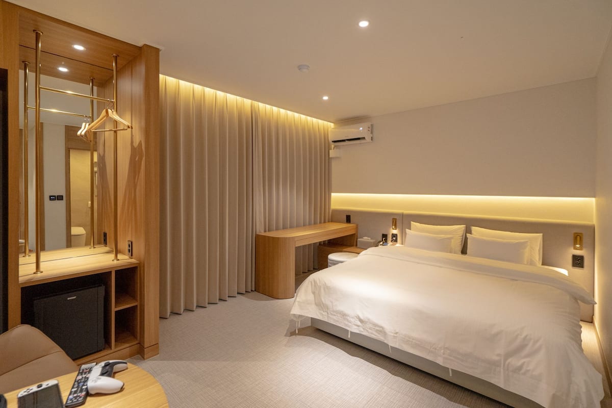 Une chambre d’hôtel moderne équipée d’un grand lit, d’un bureau avec une chaise, d’un miroir et d’une armoire.