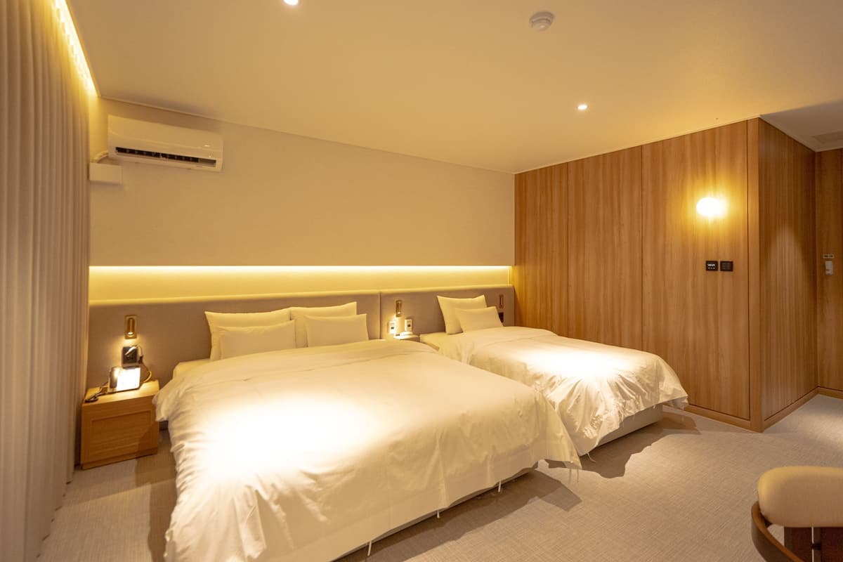 Une chambre d’hôtel avec deux lits, une table de chevet, un appareil de climatisation et un mur recouvert de panneaux en bois.