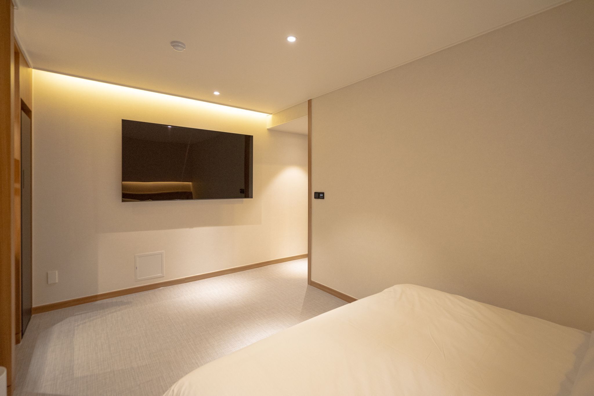 A modern hotel room with a large bed, a built-in bench, and a wall-mounted TV.