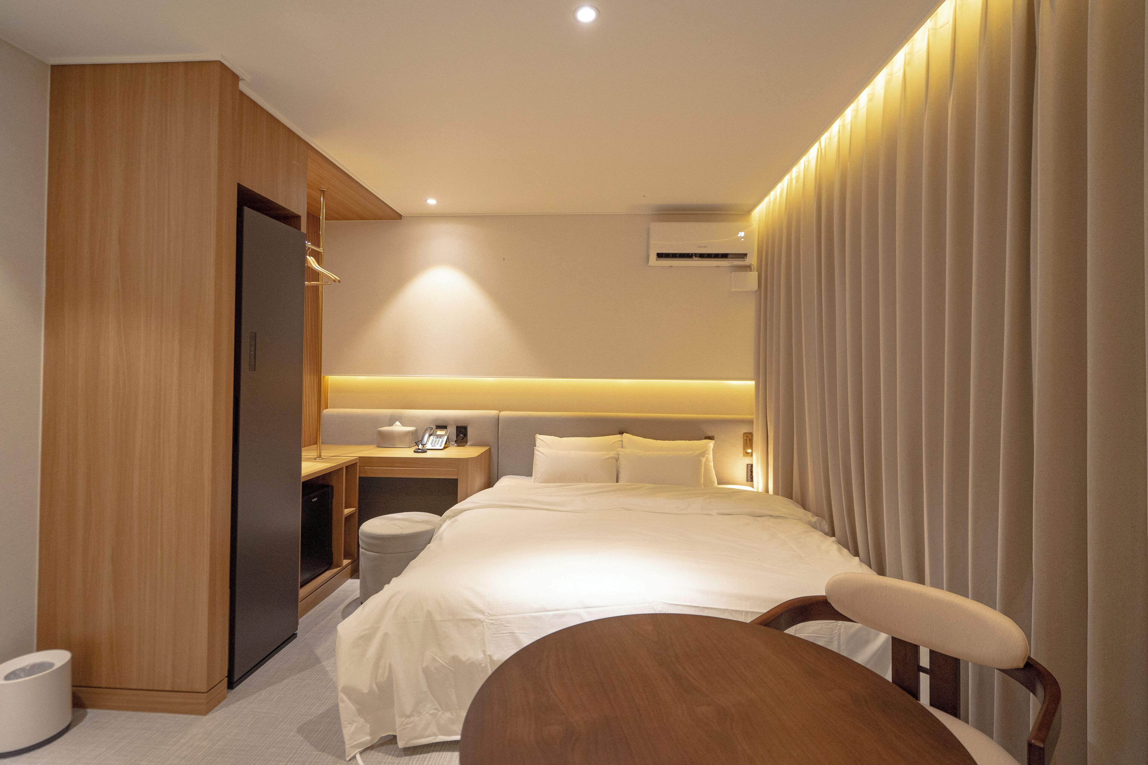 Une chambre d’hôtel moderne équipée d’un lit, d’une table de chevet, d’une chaise et d’une armoire en bois.