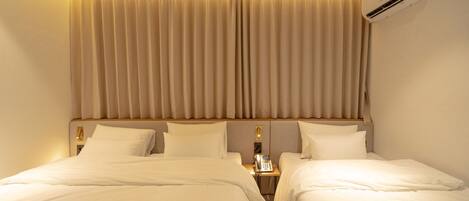 A hotel room with two beds, a nightstand with a phone, and an air conditioning unit on the wall.