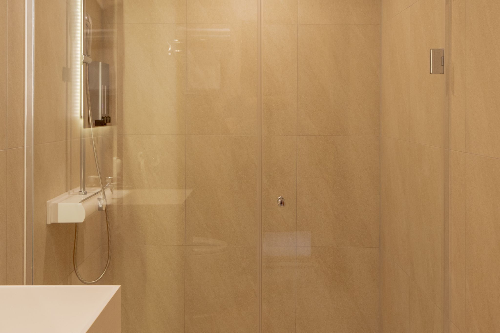 A modern bathroom with a glass-enclosed shower, a white sink, and a beige tiled wall.