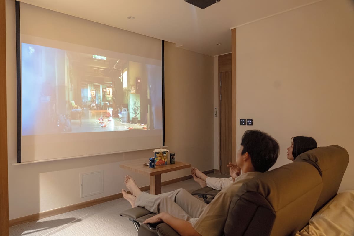 Un salon avec un grand écran diffusant un film, un canapé et une table basse avec des boissons.
