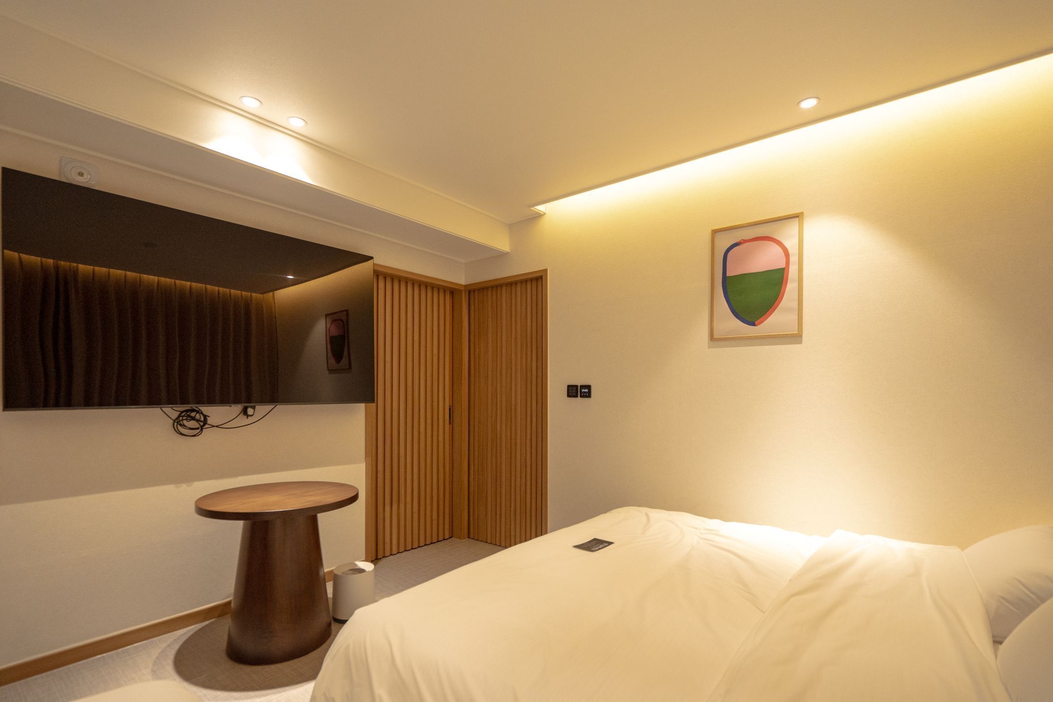 Une chambre d’hôtel moderne avec un lit, une table ronde en bois, un petit lavabo et un miroir.