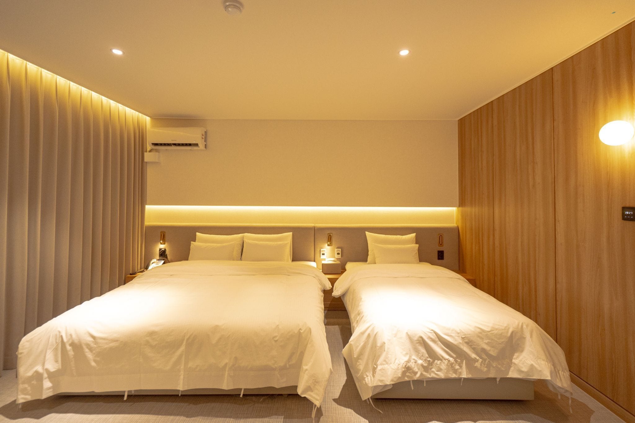 Habitación de hotel con dos camas, un panel de pared de madera, una lámpara en el techo y un equipo de aire acondicionado.