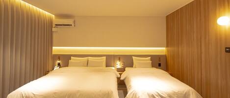 A hotel room with two beds, a wooden wall panel, a ceiling light, and an air conditioning unit.