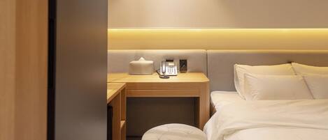 A hotel room with a bed, a bedside table with a lamp, a telephone, and a small ottoman.