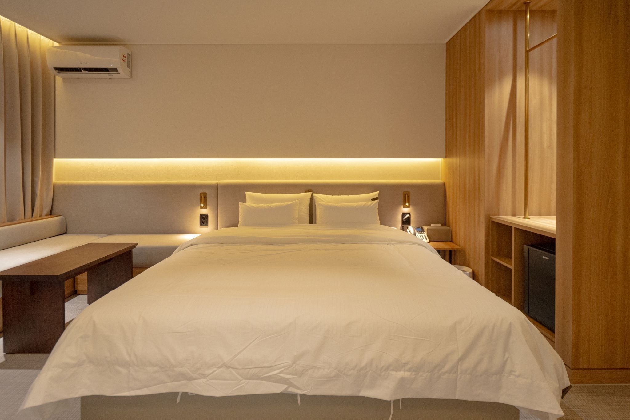 Una habitación de hotel moderna con una cama grande, mesitas de noche, un banco y un armario empotrado.