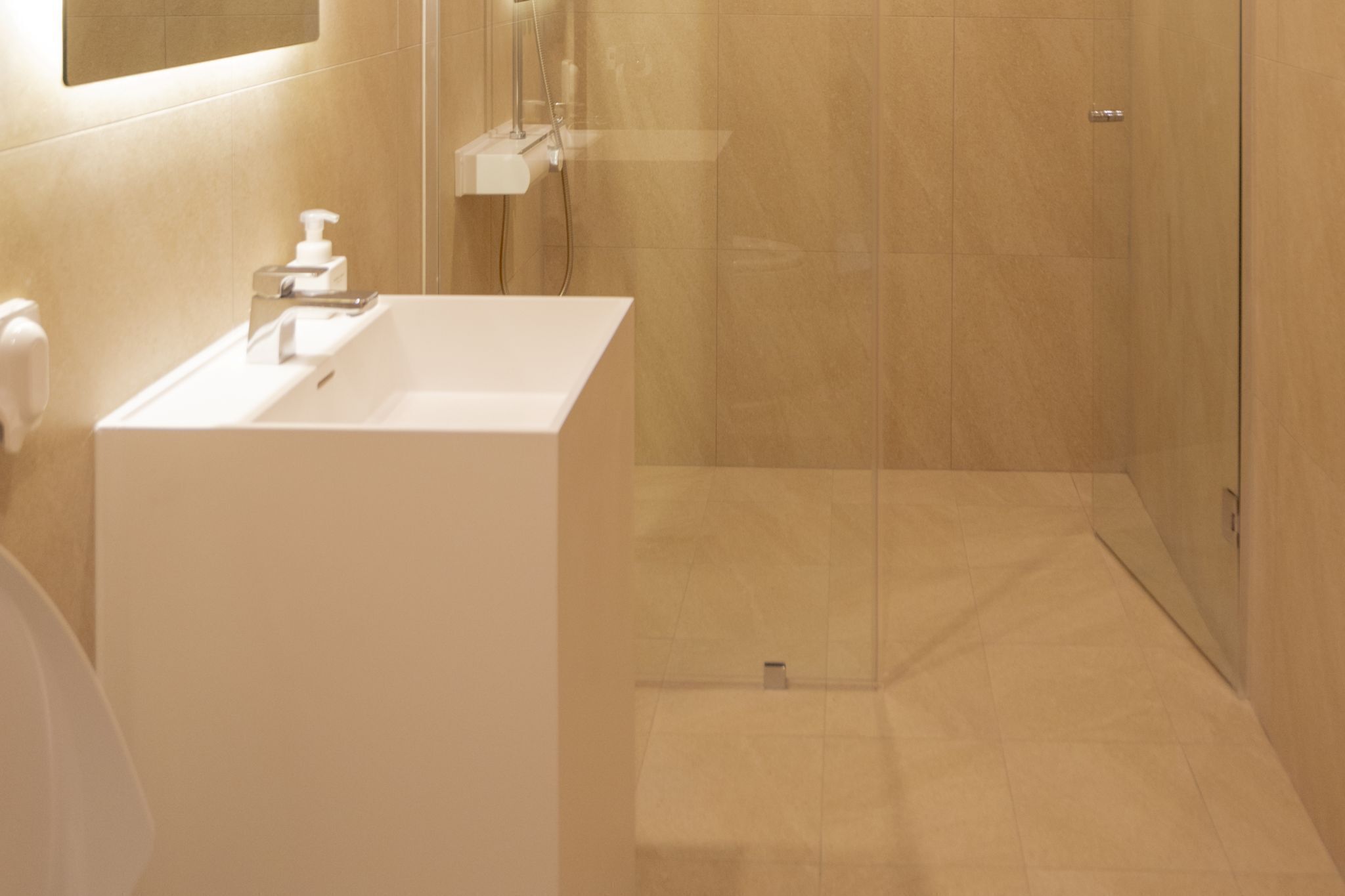 A modern bathroom with a white sink, a mirror, and a shower area.