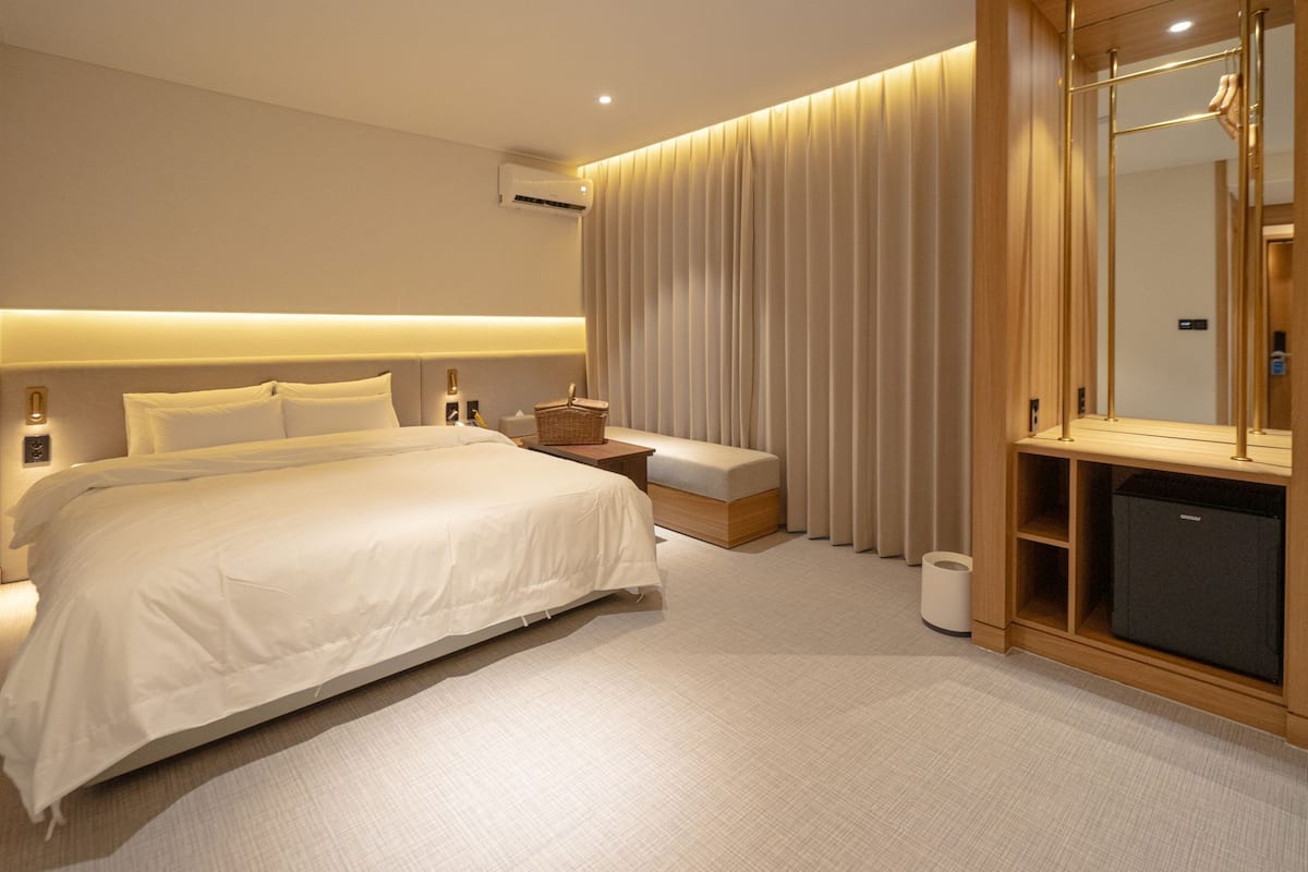 Une chambre d’hôtel moderne avec un grand lit, des tables de chevet, un banc, une armoire et un miroir.