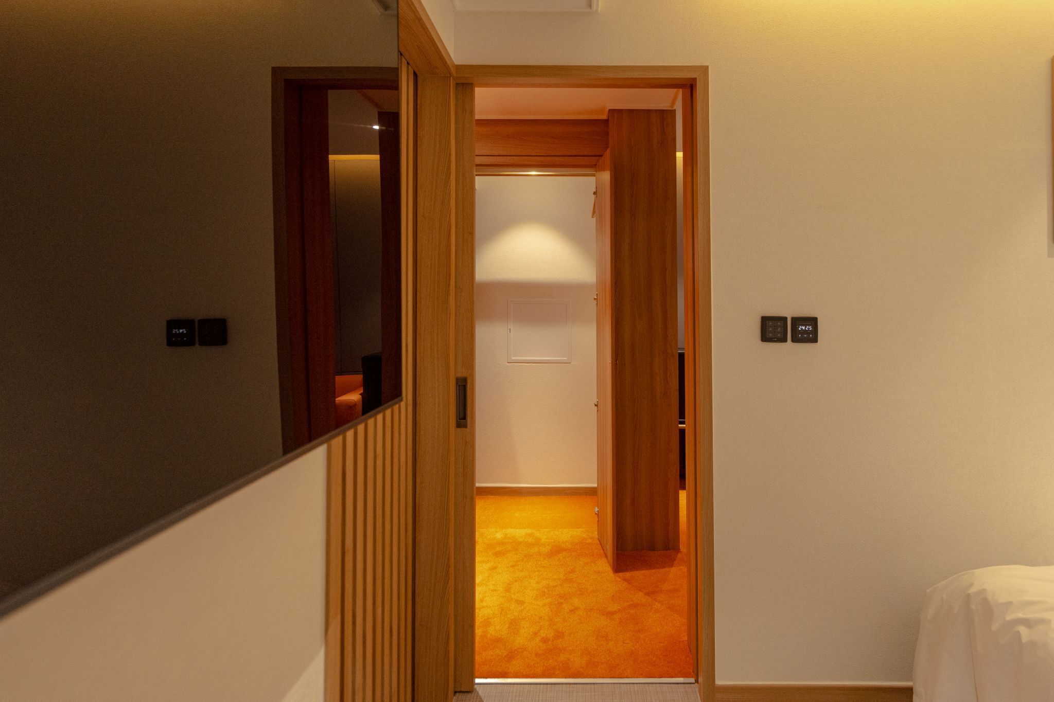 A hallway with wooden doors leading to a room with a carpeted floor.