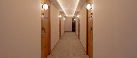 A hotel hallway with carpeted floors, wooden doors, and wall-mounted lights.