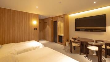 Habitación de hotel con dos camas, una mesa de comedor con sillas, un televisor de pantalla plana en la pared y un panel de pared de madera.