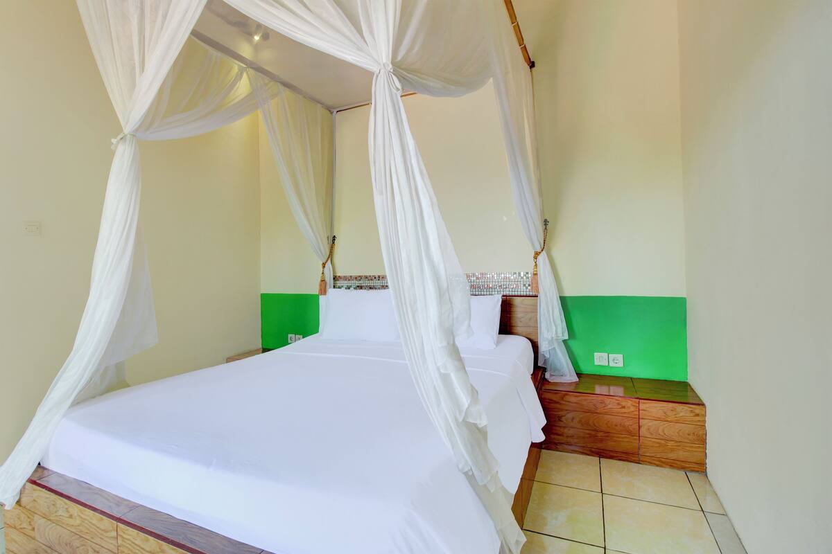 A room with a bed under a white canopy, a green wall, and a wooden nightstand.