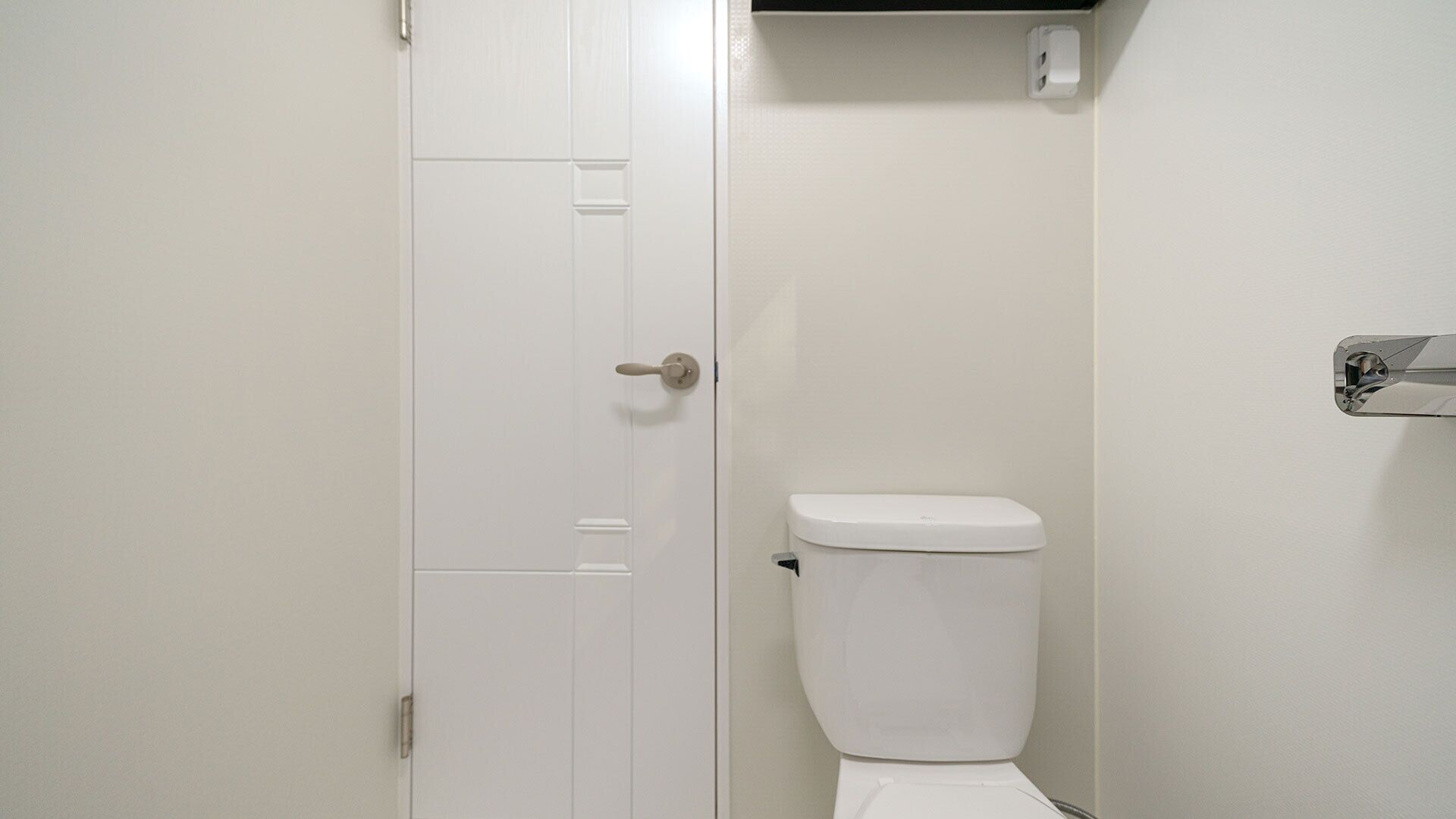 Ein kleines, weißes Badezimmer mit geschlossener Tür und Toilette.