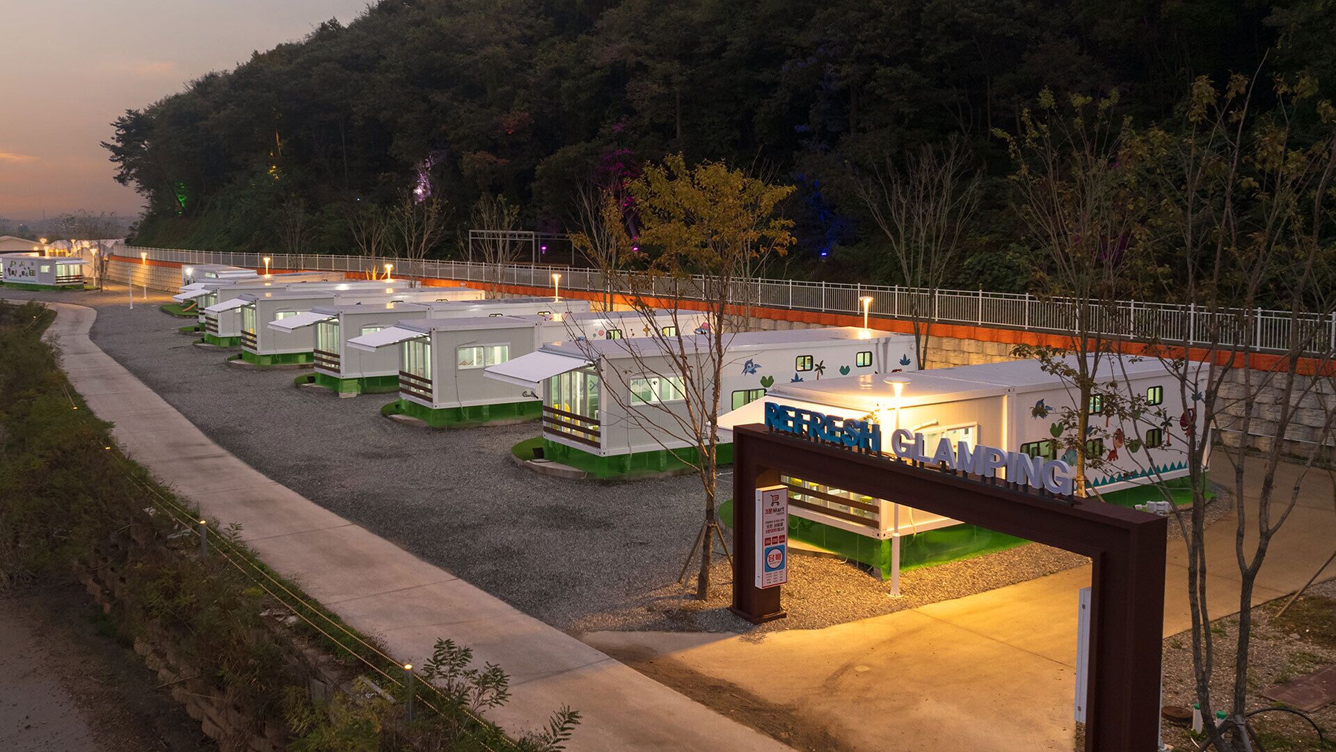 A row of small, modern cabins with a sign reading "REFRESH CLAMPING" in a campground setting.
