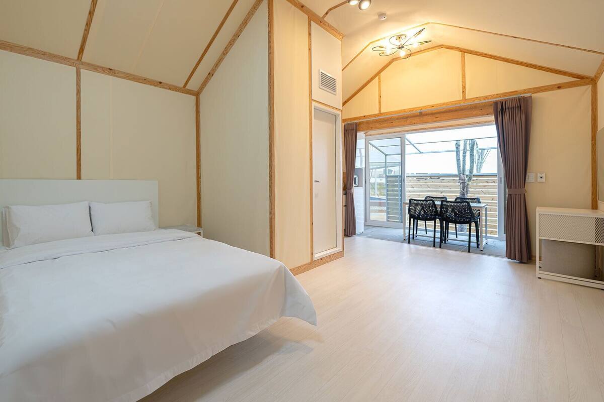 Ein Schlafzimmer mit einem Bett, einem Schreibtisch und einem Stuhl. Eine Glastür führt zu einem Außenbereich.