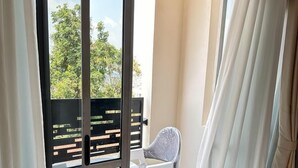 A balcony with a white chair, a small table, and a sofa with an orange pillow. - LivLuxe Apartments 2 (Kampala)