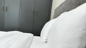 A neatly made bed with white linens and pillows, grey wardrobe with handles, and a grey headboard. - LivLuxe Apartments 2 (Kampala)