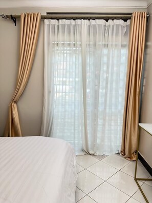 A hotel room with a bed, curtains, and a window with blinds.