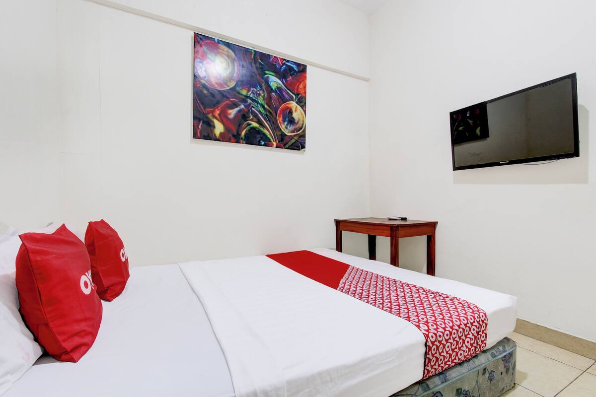Une chambre d’hôtel avec un lit, une télévision, un tableau et une petite table.