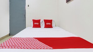 Un lit avec une literie blanche et rouge, deux oreillers rouges ornés du texte « OYO », une porte grise et un mur blanc uni.
