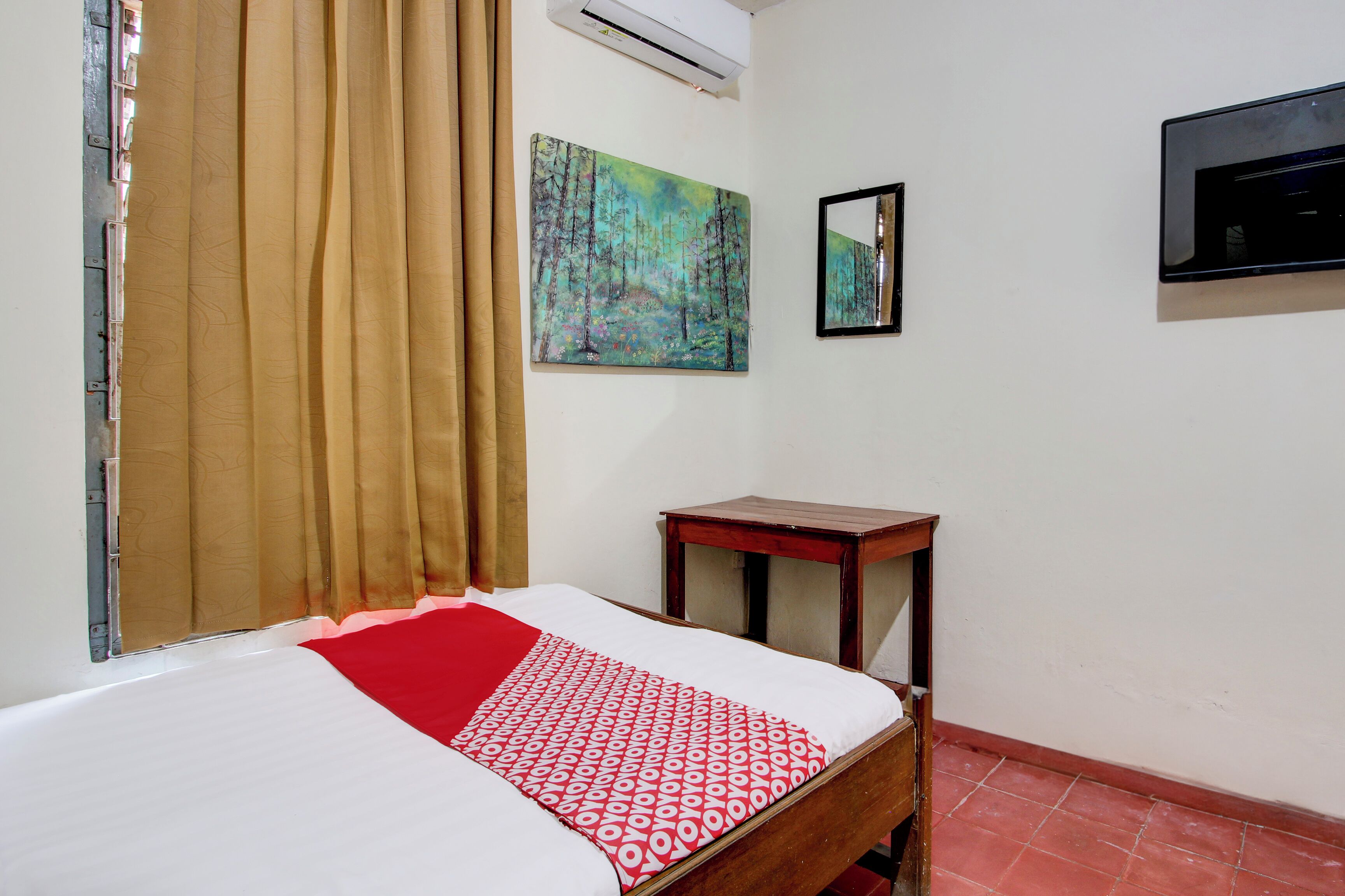 A room with a bed, a small wooden table, a mirror, and a painting on the wall.