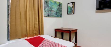 A room with a bed, a small wooden table, a mirror, and a painting on the wall.