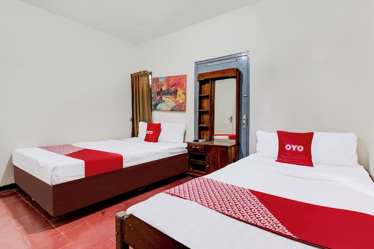 Une chambre d’hôtel avec deux lits, chacun agrémenté de draps blancs et de touches de couleur rouge, une armoire en bois, un miroir et un tableau au mur.