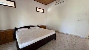 A bedroom with a single bed, wooden headboard, two bedside tables, a small bedside lamp, and an air conditioning unit on the wall. - Hotel O Gunung Mas Homestay (Pemuteran)